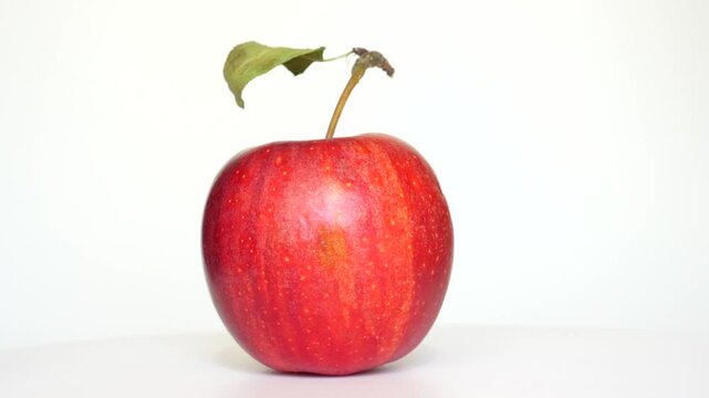 Vibrant red apple featuring a green leaf on top, set against a clean white background in a spin video.