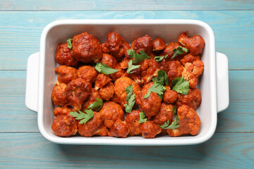 Baked cauliflower buffalo wings with parsley in baking dish on light blue wooden table, top view