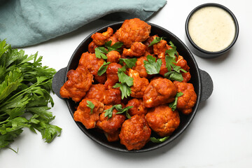 Baked cauliflower buffalo wings in baking dish, parsley and sauce on white table, top view