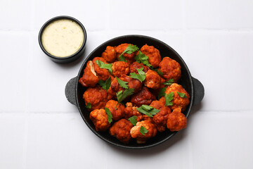 Baked cauliflower buffalo wings with parsley served on white tiled table, flat lay
