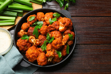 Tasty cauliflower buffalo wings, sauce and celery on wooden table, flat lay. Space for text