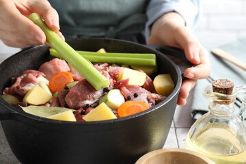 Woman preparing stew with vegetables and meat at white tiled table, closeup