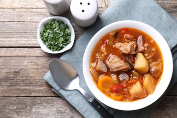 Delicious stew with vegetables in bowl, parsley and spoon on wooden table, top view