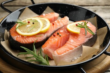Fresh raw salmon steaks with spices in pan on wooden table, closeup
