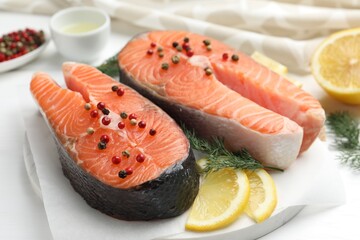 Fresh raw salmon steaks with peppercorns, lemon and dill on white table, closeup