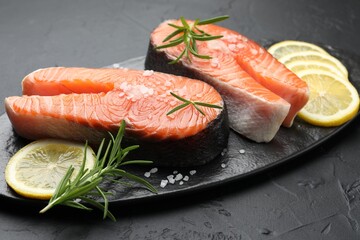Fresh raw salmon steaks with salt, lemon and rosemary on dark textured table, closeup