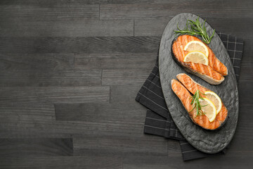 Tasty grilled salmon steaks with lemon and rosemary on dark wooden table, top view. Space for text