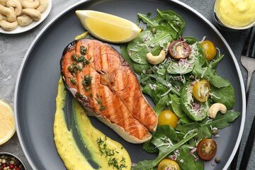Tasty grilled salmon steak with lemon, sauce and salad served on grey table, flat lay
