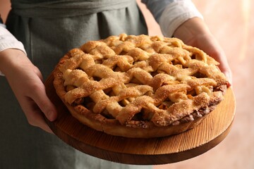Woman holding wooden board with tasty homemade apple pie on light background, closeup