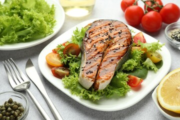Tasty grilled salmon steak with vegetables served on light grey table, closeup