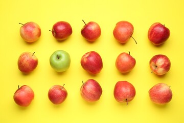 Flat lay composition with green apple surrounded by red ones on yellow background