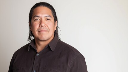 Obraz premium Mature native american male with long black hair wearing a collared shirt is posing for a portrait in front of a white backdrop