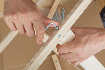 close-up： one hand holds a hex key in a confirmat screwed into a wooden table leg, the other hand holds a wooden table leg