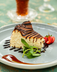 Slice of plain new york style cheesecake drizzled with chocolate syrup