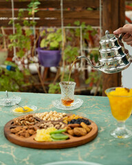 Pouring tea into crystal glass on table with nuts and dried fruits