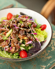 Warm salad with grilled duck breast and sesame seeds being served in a bowl