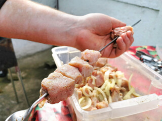 Meat in a marinade with pepper is put on a skewer, and against the background, the hand of a man with vitiligo puts a piece of meat on a skewer. Cooking a barbecue. Outdoor kitchen. Meat dish