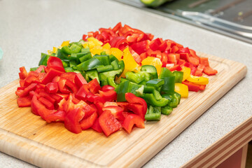 Wooden cutting board with freshly cut green, yellow, red paprika, peppers on the kitchen countertop. Close-up view. Healthy food cooking, home made healthy dinner. Fresh vegetables