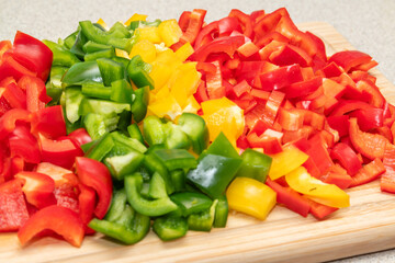 Wooden cutting board with freshly cut green, yellow, red paprika, peppers on the kitchen countertop. Close-up view. Healthy food cooking, home made healthy dinner. Fresh vegetables