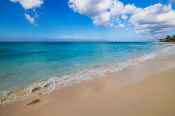 Sunny day at calm beach in Aruba with gentle waves washing up on soft sand under bright blue sky.