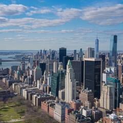 Obraz premium Aerial view of Manhattan skyline with numerous skyscrapers under a blue sky with scattered clouds.
