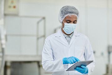 Medium shot of African American male manufacturing supervisor working at pharmaceutical factory using digital tablet to monitor production process, copy space