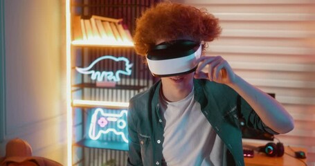 Excited teen boy looking at camera and put on  VR headset on his head walking around the room  with outstretched arms to maintain a balance beam while playing a virtual video game