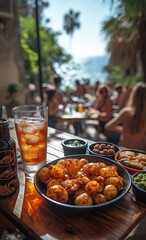 Close-up of food and drinks on a terrace with a view of palm trees and mountains in the distance. Sunny day, pale blue sky, Mediterranean setting, Europe.