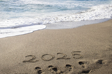 tropical New Year 2025 written in sand on the beach