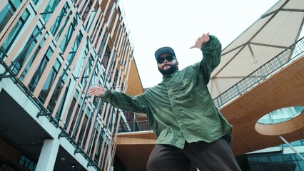 Low angle view of hipster pose in hip hop style surrounded by mall view. Portrait of sporty asian hip hop choreographer dancing break dance while looking at camera. Outdoor sport 2024. Hiphop.