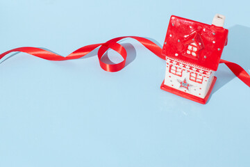 Miniature house and red ribbon on bright blue background. Christmas holiday concept.