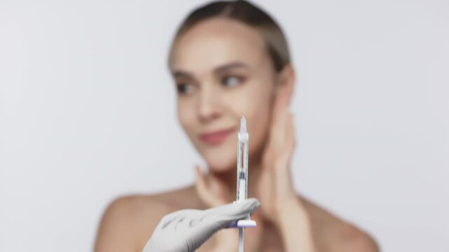 A young, beautiful woman stands against a white background, enjoying her beauty as a syringe appears in front of her. This image embodies self-confidence and the realm of cosmetic procedures.