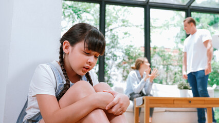 Obraz premium Stressed and unhappy young girl huddle in corner, cover her ears blocking sound of her parent arguing in background. Domestic violence at home and traumatic childhood develop to depression. Synchronos