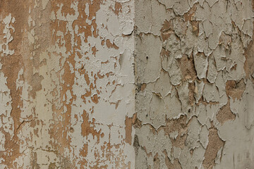 Detailed close-up of cracked, peeling white paint on a rough textured wall, exposing the underlying brown surface. The texture highlights decay and aging.