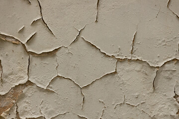 Detailed close-up of cracked, peeling white paint on a rough textured wall, exposing the underlying brown surface. The texture highlights decay and aging.