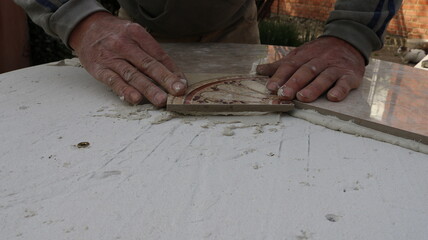 laying decorative ceramic tiles on a table surface to create a tile pattern of geometric pieces, the manual skill of a furniture designer, hands pressing on ceramic material lying on a layer of mortar