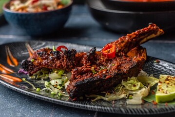 Spicy grilled lamb chops with vegetable salad, red chili, and tomato served on a dinner table