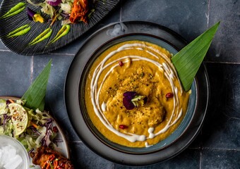 Roasted butternut chicken squash soup decorated with maroon and yellow flowers, and pomegranate served on a dinner table with more mouthwatering foods