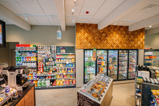 A convenience store interior with stocked shelves of snacks, drinks in coolers, car care products, and a freezer with food items.