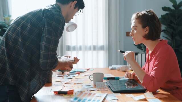 Top view of smart designer holding color palette while project manager looking at design and choosing color for program. Professional businesswoman taking a note while design creative logo. Symposium.