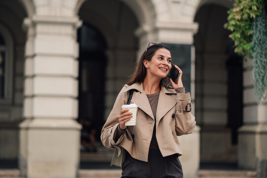 Smiling businesswoman walking and talking on the phone holding coffee