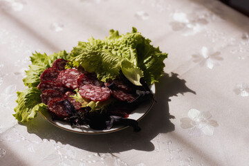 Sliced smoked sausage and leaves of greens on a plate on the table with a tablecloth