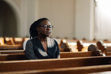 Black woman praying sitting on bench in church