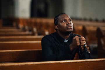 Priest praying with rosary beads in church pew