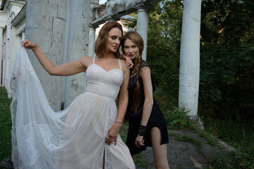 Fototapeta premium Two beautiful girls, sisters Lilith and Eva, pose in rocking dresses against the background of columns.