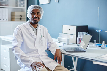 Medium portrait shot of African American male lab chemist in medical hairnet smiling at camera...