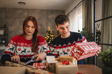 Adult young couple wrap Christmas gift with festive decorations