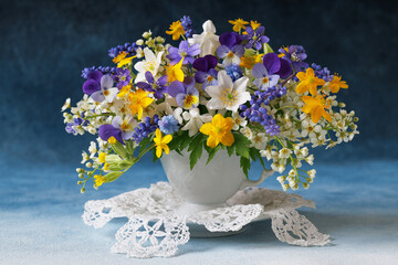 Bouquet of wild spring flowers in a cup, blue muscari, hepatica, pansies, yellow anemones, white bird cherry. Beautiful card