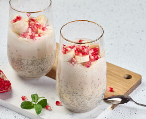 A glass of chia seeds and yogurt, with banana pieces and pomegranate seeds added to the dessert
