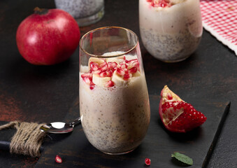 A glass of chia seeds and yogurt, with banana pieces and pomegranate seeds added to the dessert